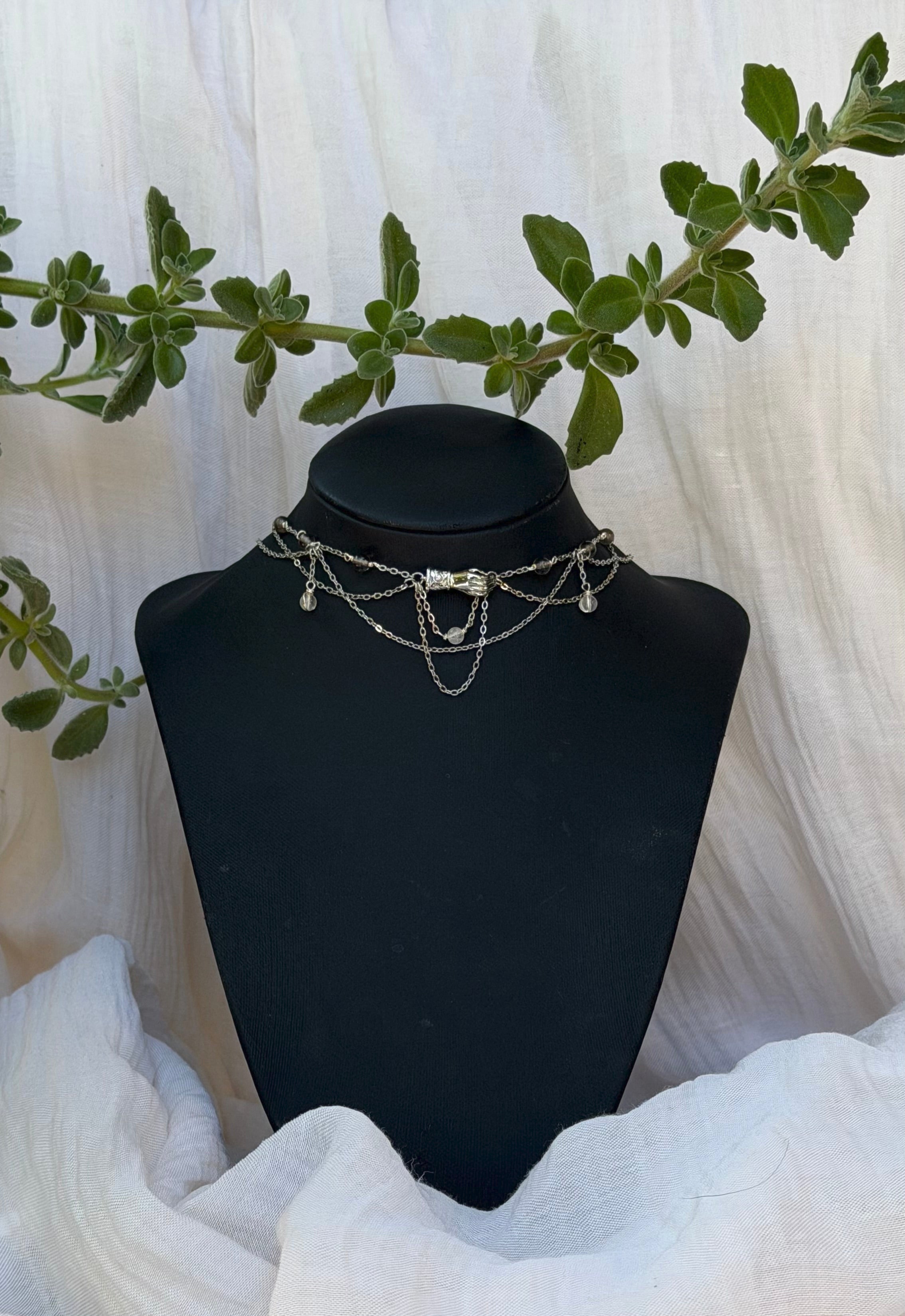 Collier La Main de la Reine, unique argenté, obsidienne de glace, cristal de roche, pendentif main
